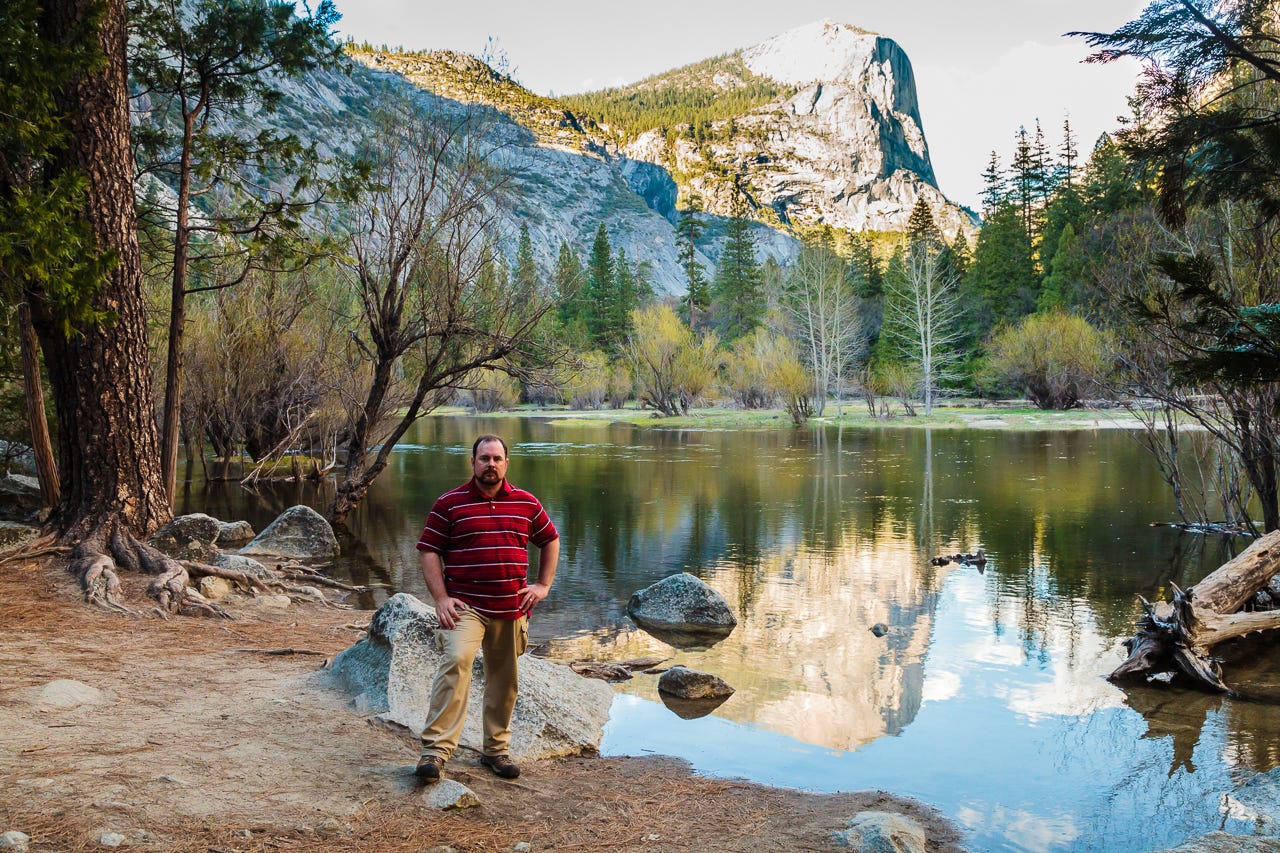A photo of a man standing in front of a small lake at Yosemites National Park, with the rear slop of Half Dome in the background. The photo is thoroughly described in this post.