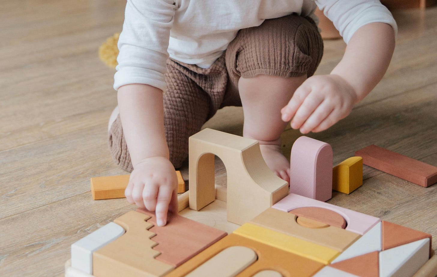 Una bambina bianca di circa due anni gioca con delle costruzioni a incastro di legno