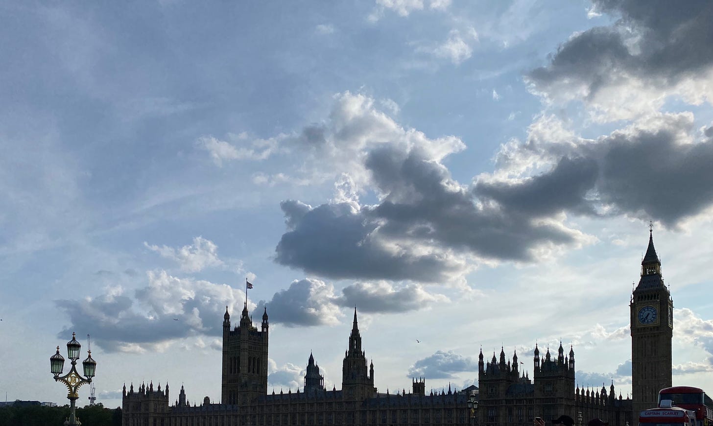 the houses of parliament silhouetted against a pale blue cloudy sky, the sharp spires contrasting with the softness of the clouds