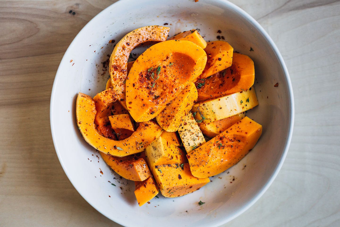 Sliced butternut squash coated with herbs and spices, in a bowl