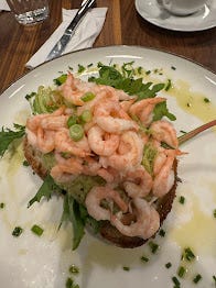 A plate with an open sandwich. Lettuce leaves on bread are covered in an absolute mountain of pink prawns.