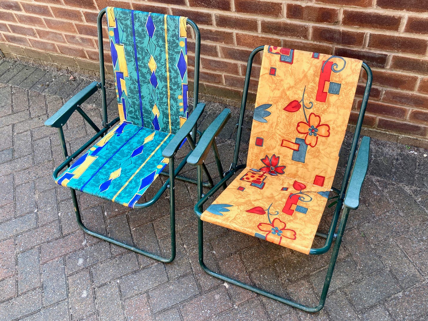 Two colourful folding garden chairs that are broken. The frames are green, and the canvas is green, blue  and yellow on one. The other is orange, red and green.