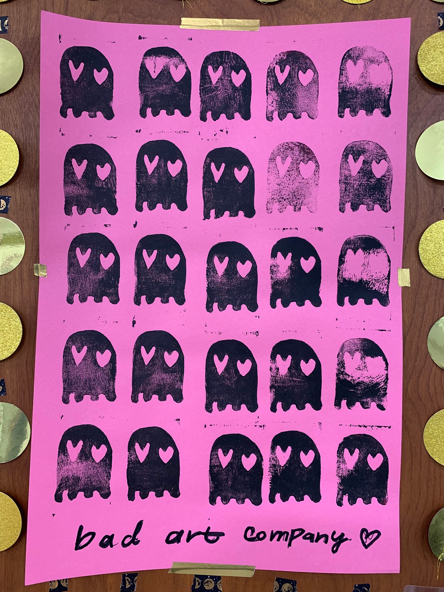 A pink poster with stamped black Pac-Man style ghosts with heart eyes on it.