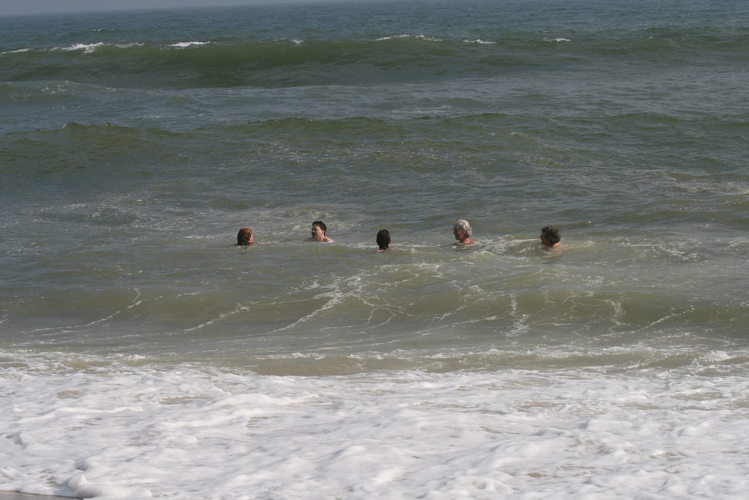 Five people swimming in the water, just beyond where the waves are breaking, heads just visible.