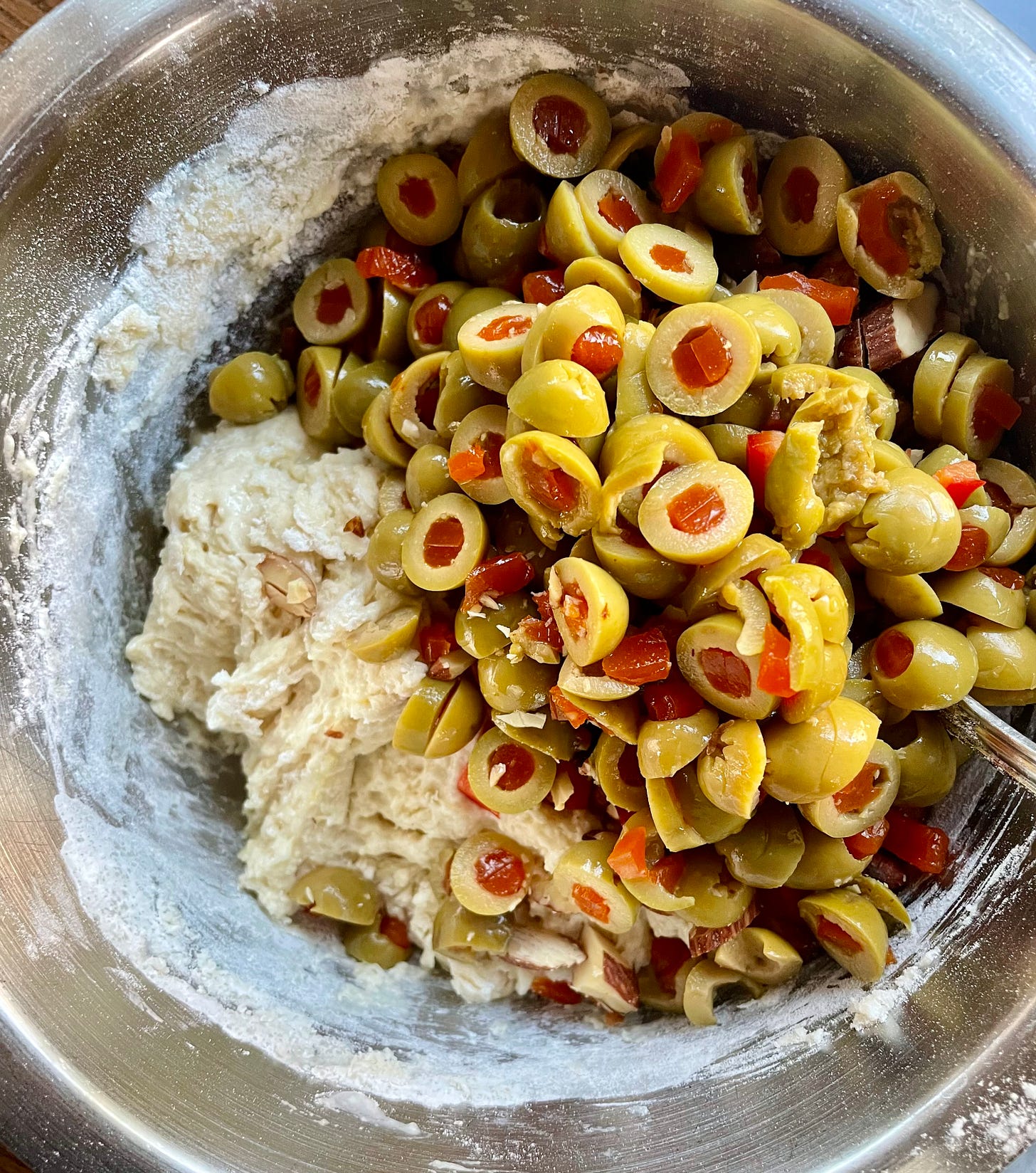 A mountain of green olives atop a mound of sticky dough.