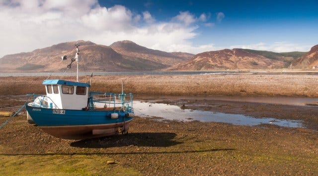 Small blue boat stranded a dry lake with mountains in the background