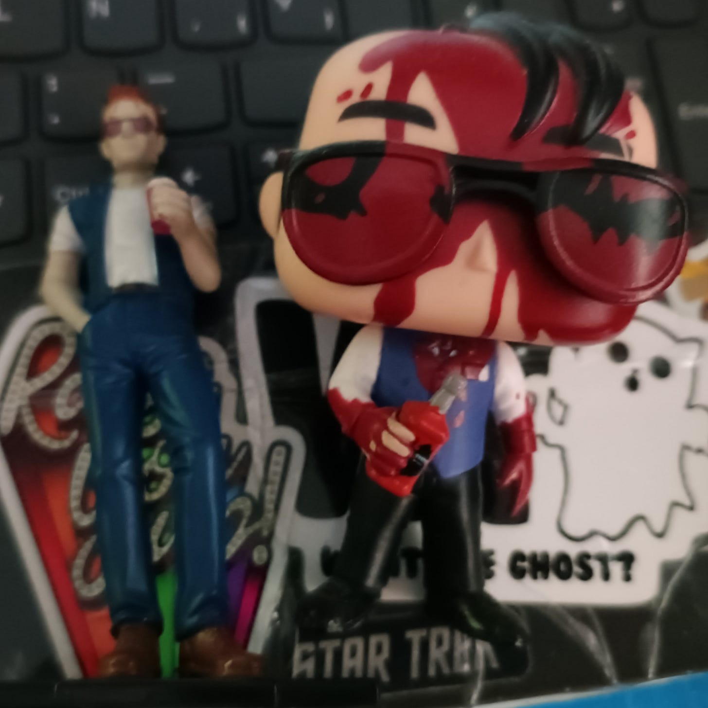 Mi mini colección de Cassidys: a la izquierda, un muñeco de resina de la versión del cómic (un hombre flacucho pelirrojo con gafas de sol, chaleco y pantalones vaqueros y camisa blanca en postura chulesca que está bebiendo lo  que podría ser tanto alcohol como sangre como una combinación de ambos). A la derecha, un funko  de la serie (figura cabezona bastante mona de pelo negro despeinado, gaas de sol con una botella de  licor, un chaleco y pantalón de traje con camisa blanca; todo el recubierto de sangre, pasaron cosas en un avión)
