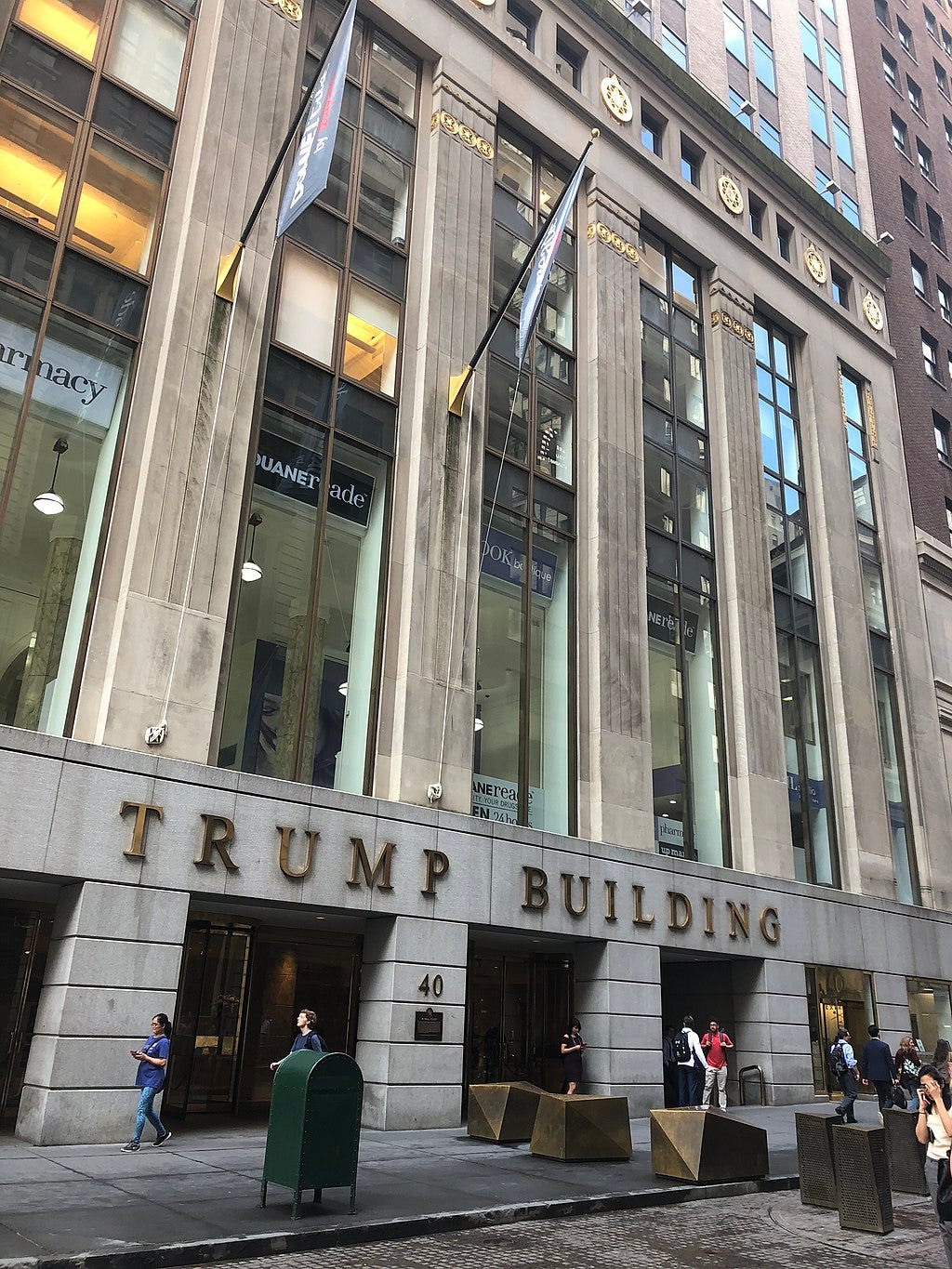 The facade of the building as seen from Wall Street. The first story is clad with granite and has several openings; the words "Trump Building" are visible above the granite columns. Above the first story are several floors of windows, which are separated by vertical stone piers.