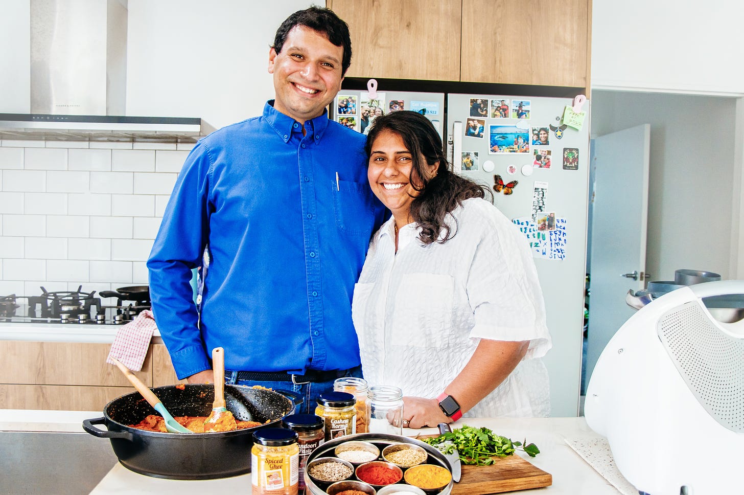 Perzen Patel and her husband in their kitchen with food on the counter top in front of them.