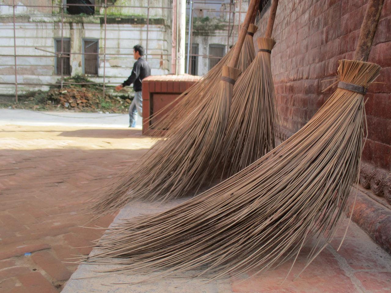 Brooms lean against a brick wall