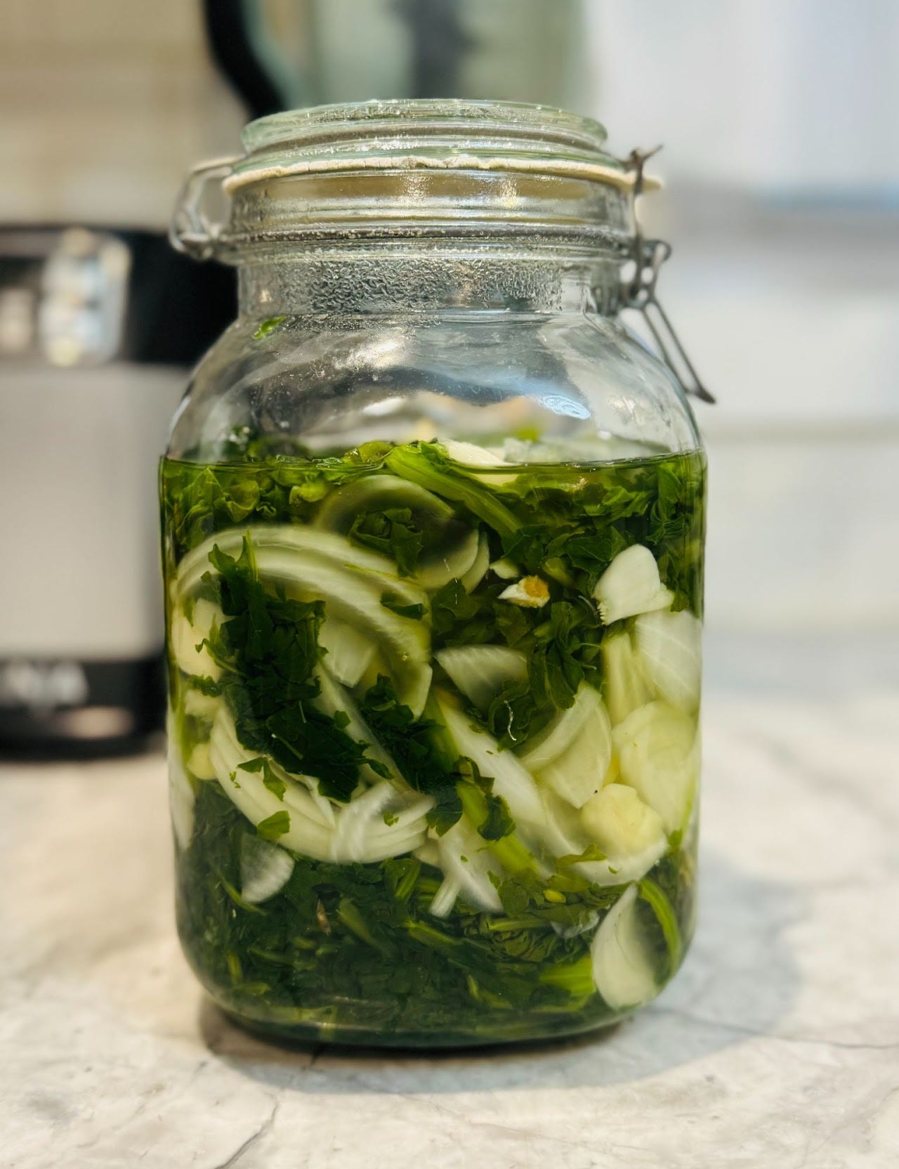 A photo of a clear mason jar holding raw sliced radishes, chopped herbs and pickling juice.
