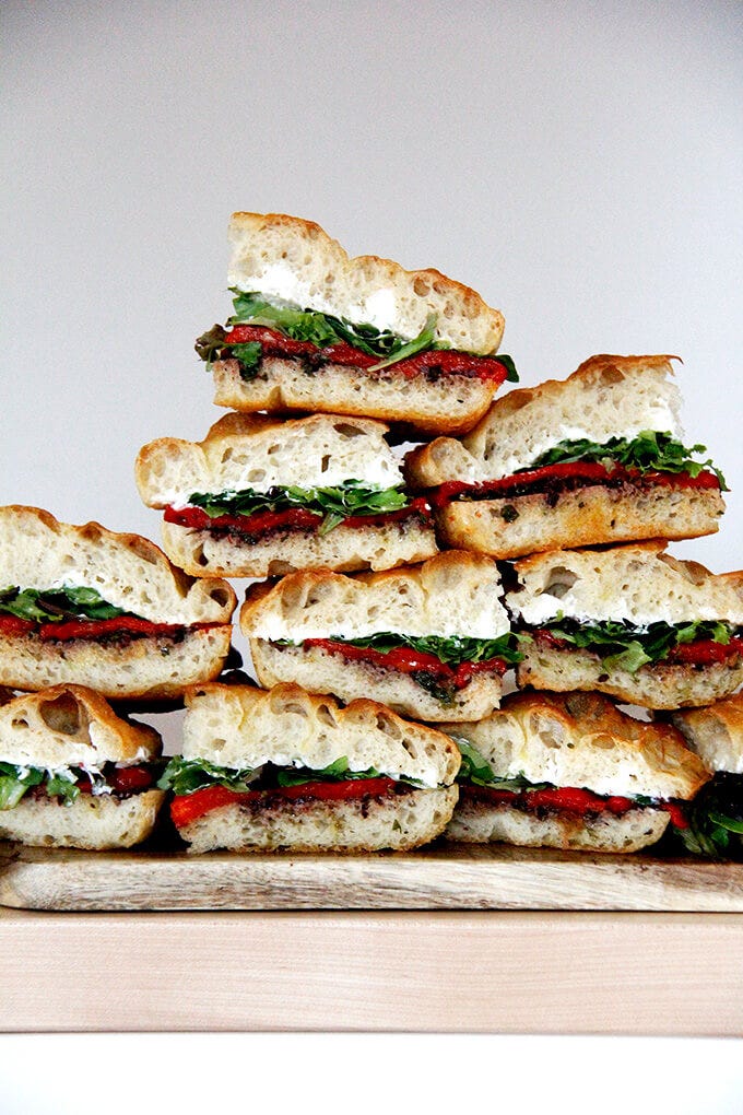 A stack of slab sandwiches with whipped honey goat cheese, roasted red peppers, olive tapenade and greens. 