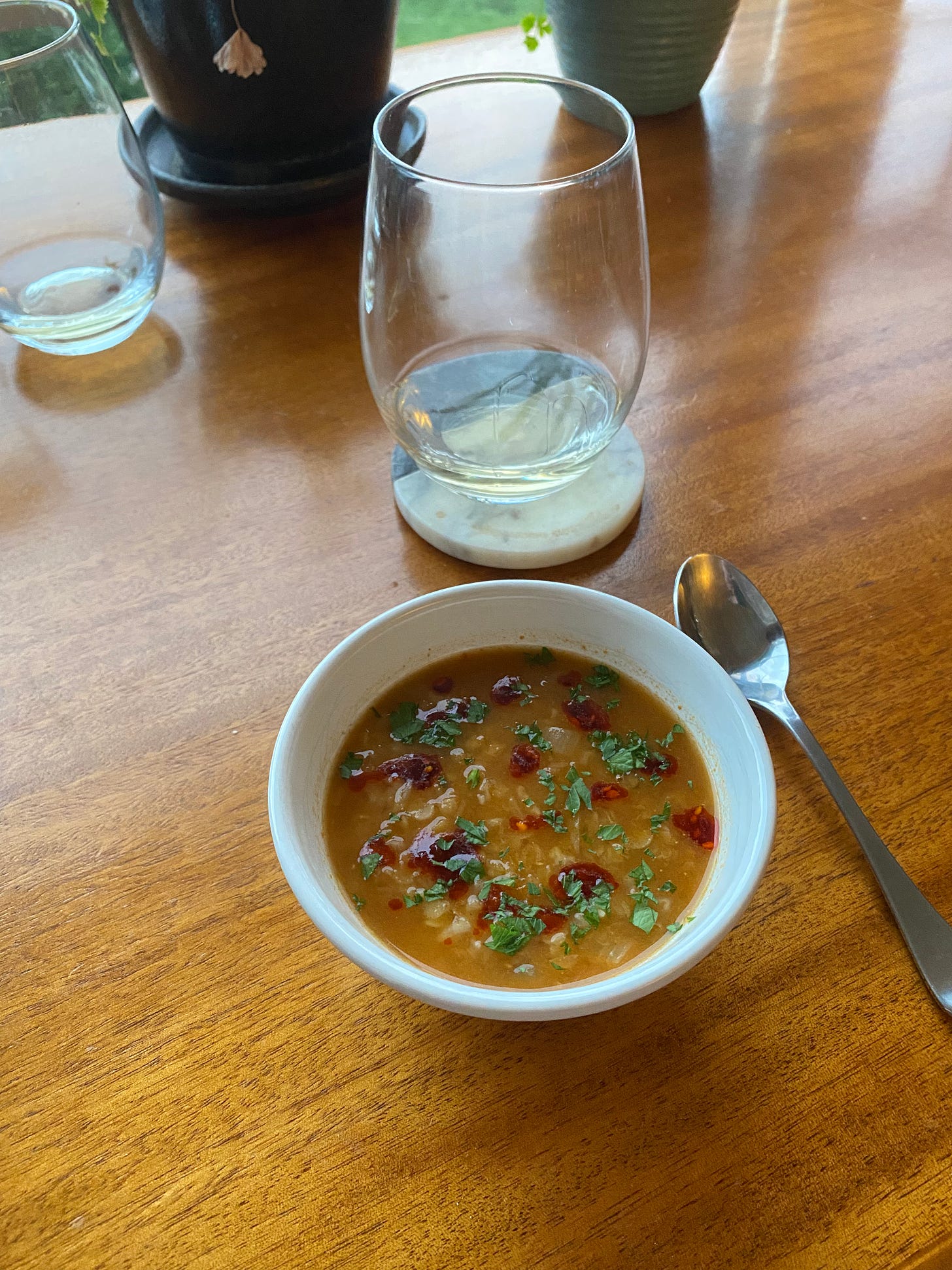 A small white bowl of the red lentil soup described above, dopped with chili crisp and chopped cilantro. There's a glass of white wine on a coaster in the background.