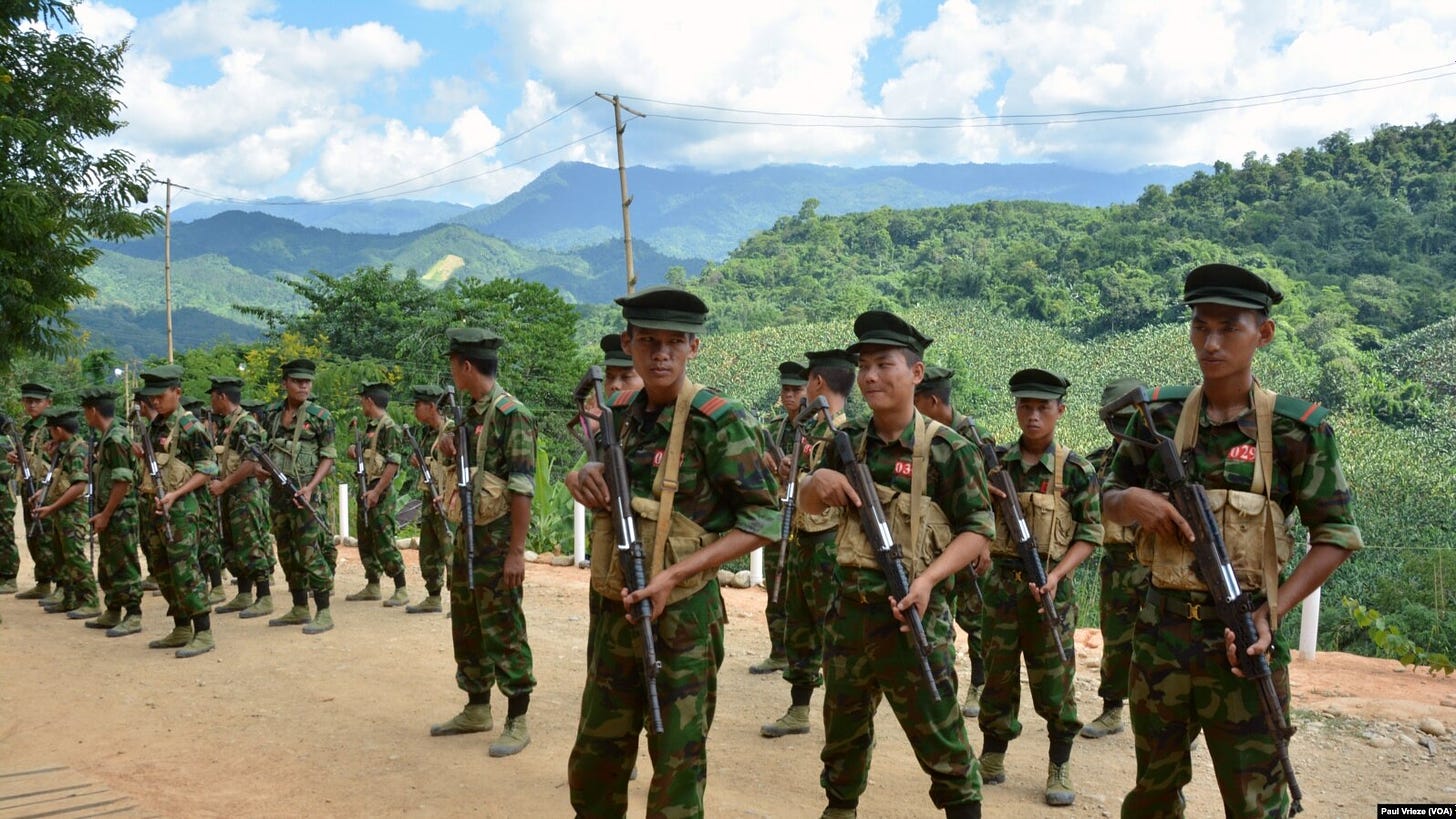 Cadets from the Kachin Independence Army stand in formation wearing great fatigues and carrying AK-47s, with the lush hills of northern Myanmar in the background.