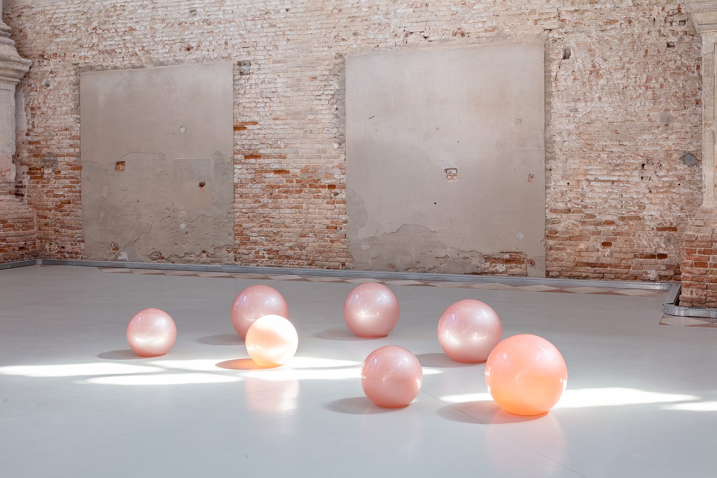 Set against a brick wall, pink and orange translucent glass balls lie on the floor.