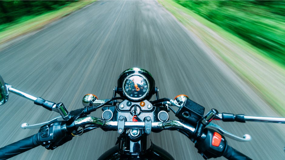 looking over the handlebars of a motorcycle as it speeds down an open road out in nature