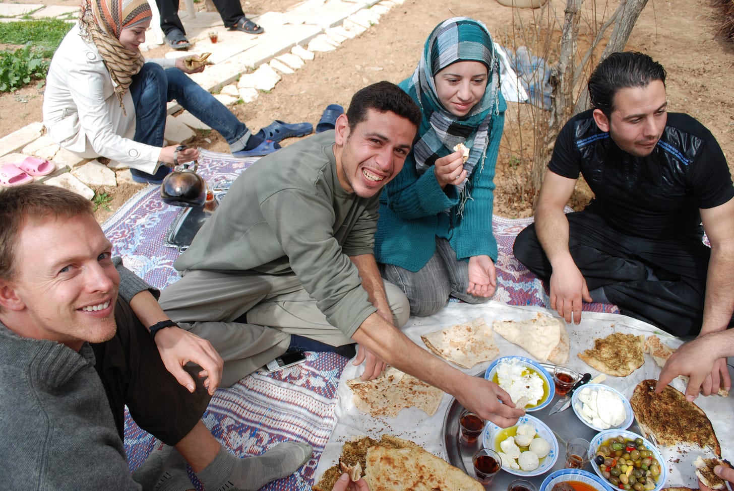 men and women sitting on the ground sharing flat bread and goast cheese and coffee in a courtyard in Syria