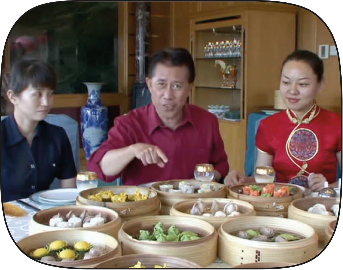 Martin Yan sitting with two women surrounded by steamers filled with elaborate dumplings.