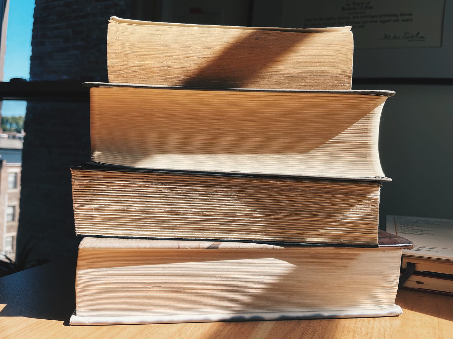 A stack of four big books on a desk, foredges facing outward