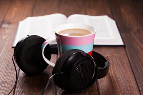 A cup of tea or coffee with a pair of headphones around it. Advertising that this is the current norm for readers