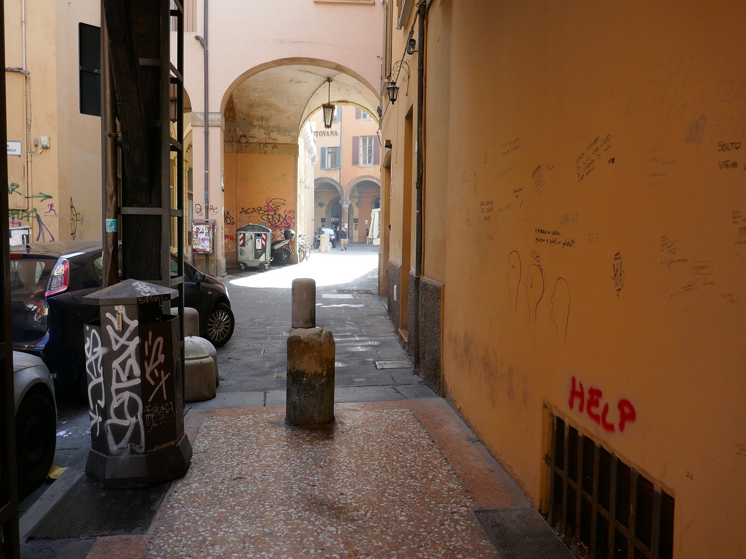 A street in Bologna with street art above a dark grate reading "Help."