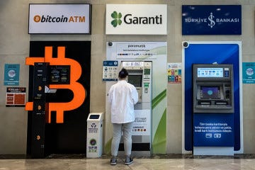 A woman uses a bank ATM next to a Bitcoin ATM machine at a shopping mall on April 16, 2021 in Istanbul, Turkey.