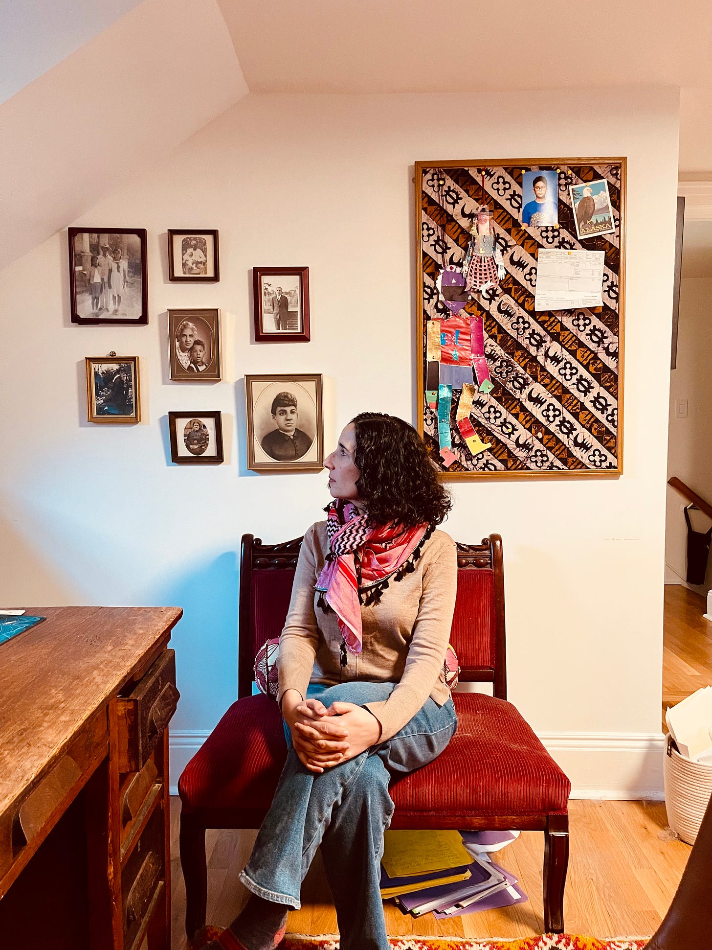 Emily Raboteau sits on a chair and looks up at her ancestor wall.