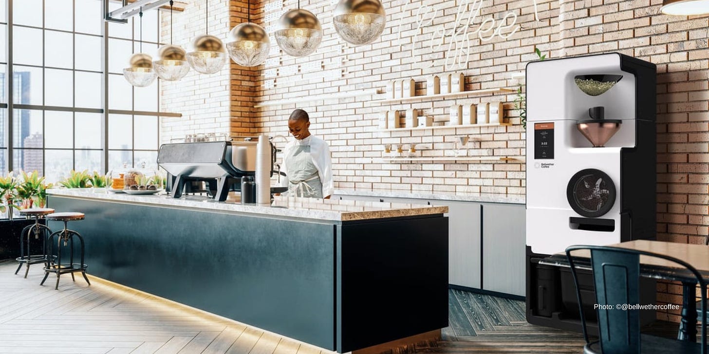 A woman pulls a shot of espresso behind a coffee bar counter in front of a brick wall. To the right of frame is a Bellwether modern, electric coffee roaster.