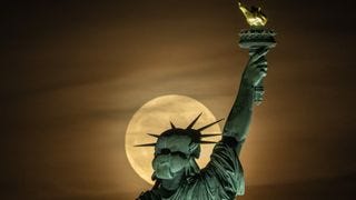 full moon shines behind the Statue of Liberty's head, looking like a halo.