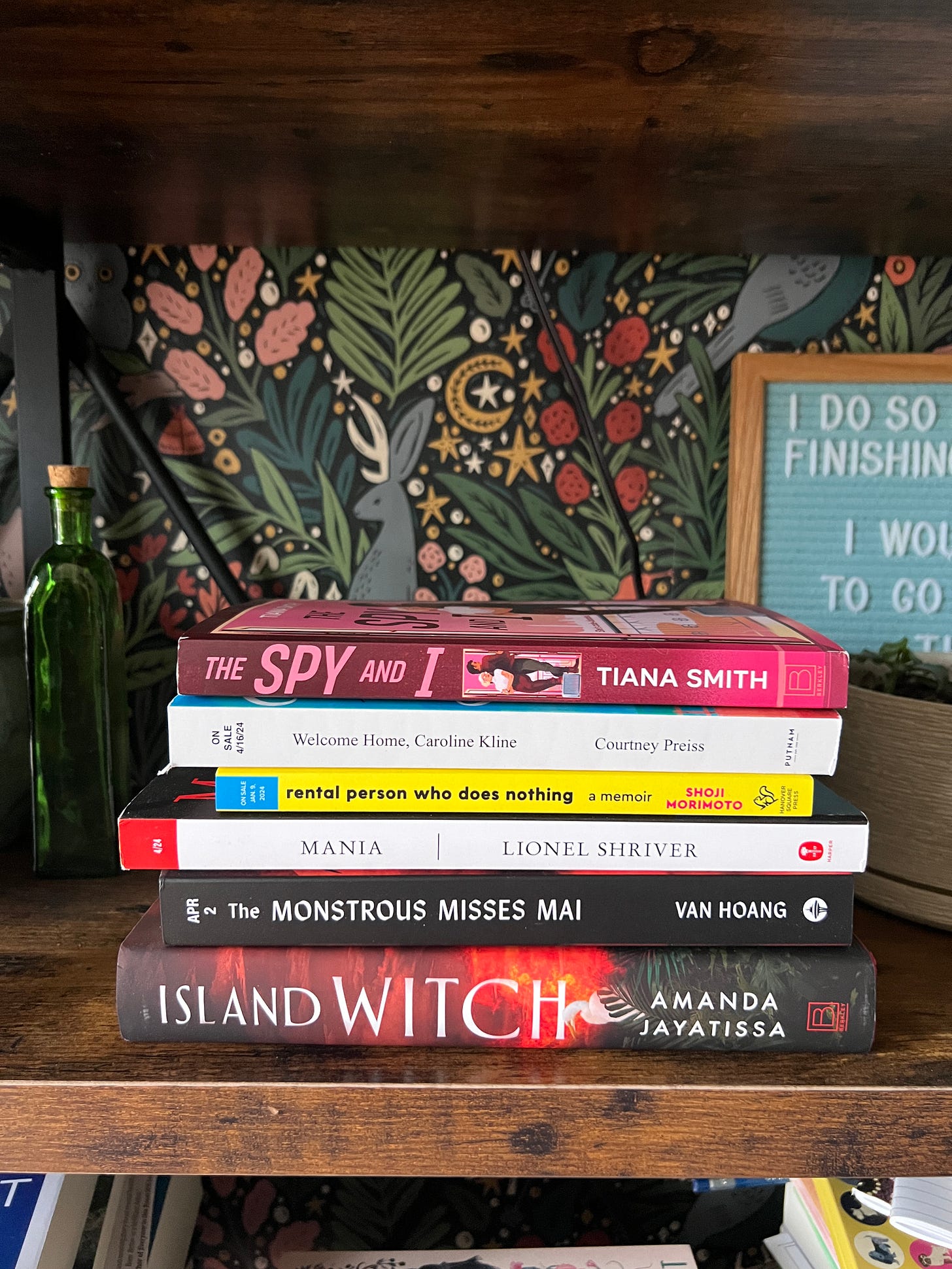 Book stack of books and ARCs that includes: The Spy and I, Welcome Home Caroline Kline, Rental Person Who Does Nothing, Mania, the Monstrous Misses Mai, and Island Witch