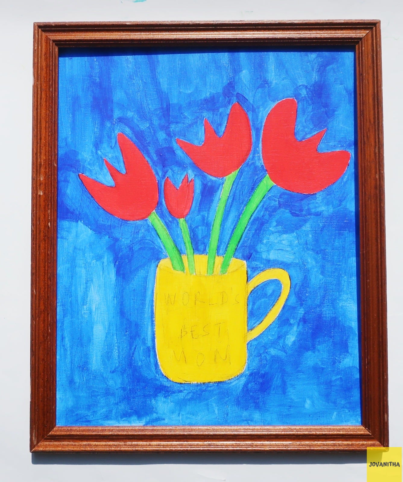 Four red tulips in a yellow mug on a blue background in a thrifted frame