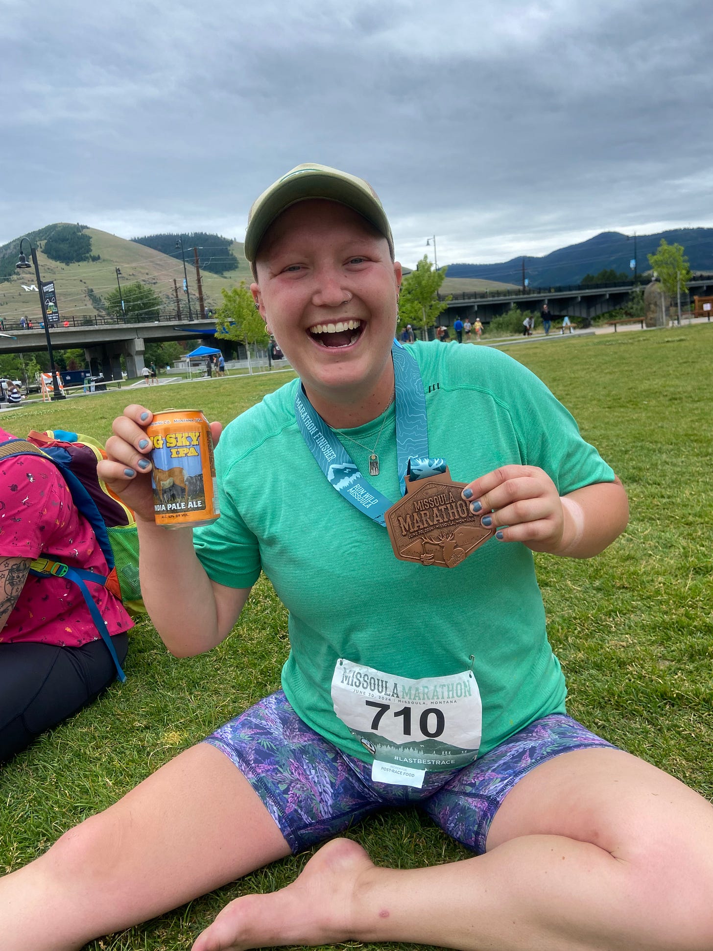 Meg Smith sits on the grass with a beer and Missoula Marathon medal. 