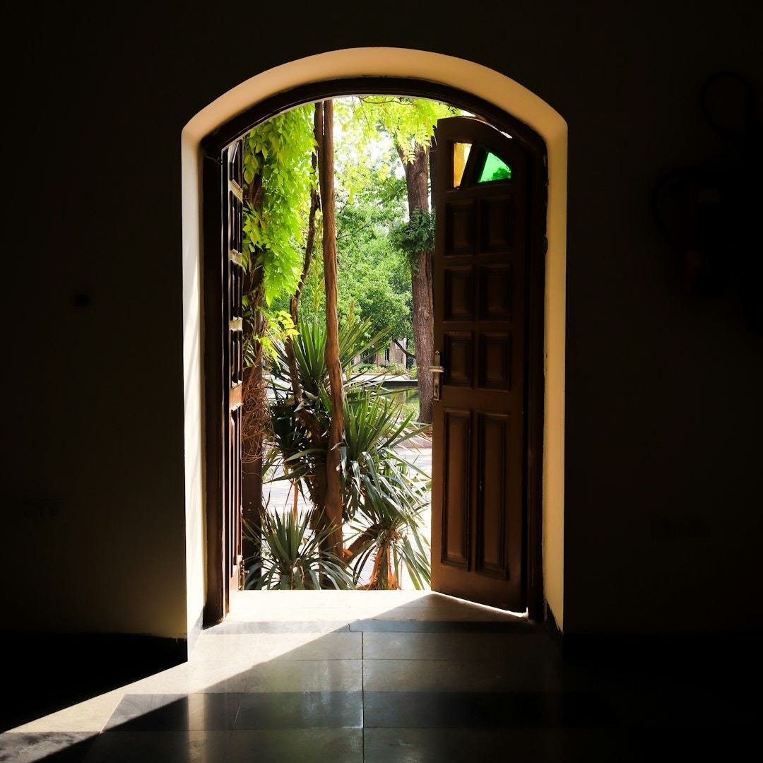 an open door leading into a lush green garden