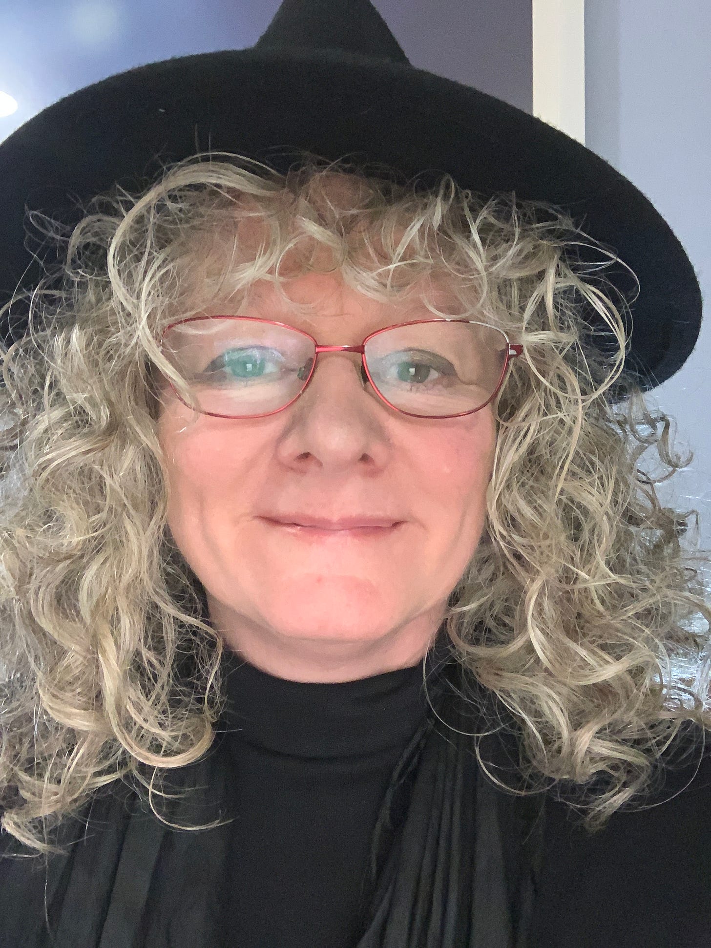 The authors face, with curly silver hair, red glasses, a black hat, and a black roll neck.