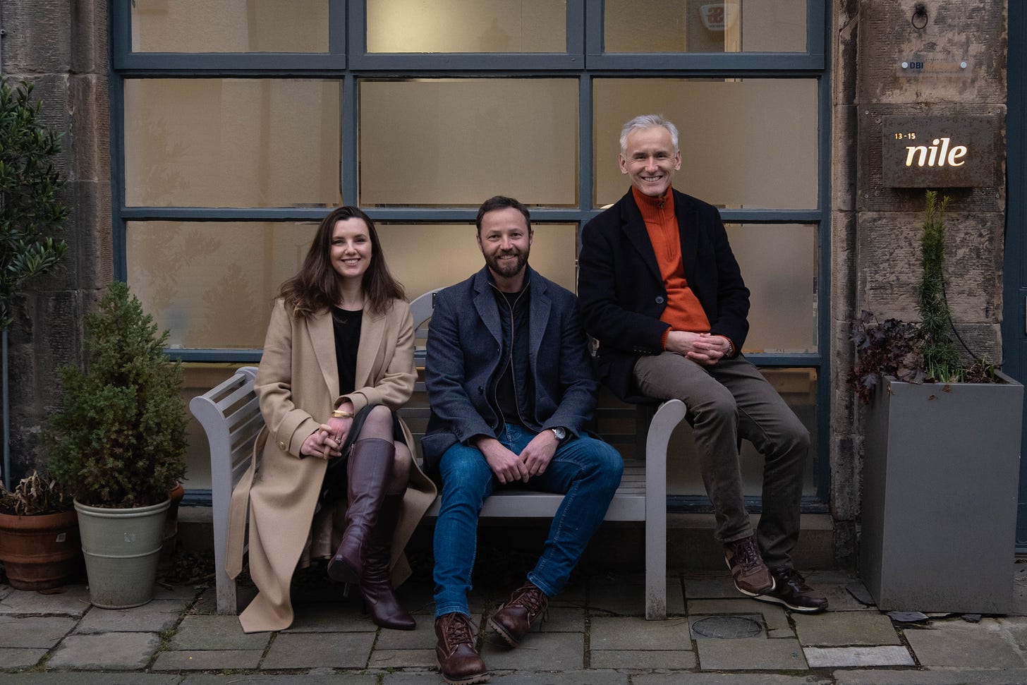 The image is a photo of members of the Nile and Dig Inclusion teams seated on a bench outside the Nile offices in Edinburgh. From left to right: Sarah Ronald, Grant Broome and Dag Lee.