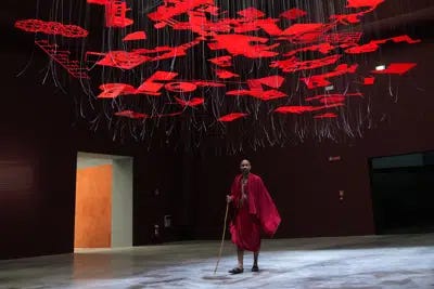 A man wearing traditional Masai clothes walks under an installation, at the Biennale International Architecture exhibition, in Venice, Italy, Wednesday, May 17, 2023. The 18th edition of the Biennale International Architecture exhibition will open to the public from Saturday May 20 to Sunday Nov. 26, 2023. (AP Photo/Antonio Calanni)