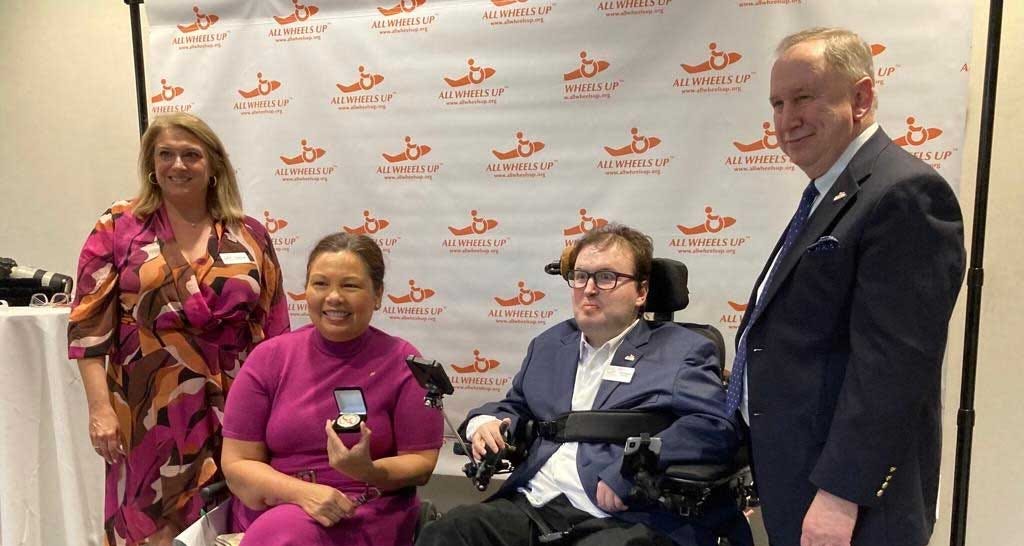 Michele Erwin and Alan Chaulet with Senator Duckworth in front of All Wheels Up step and repeat banner.