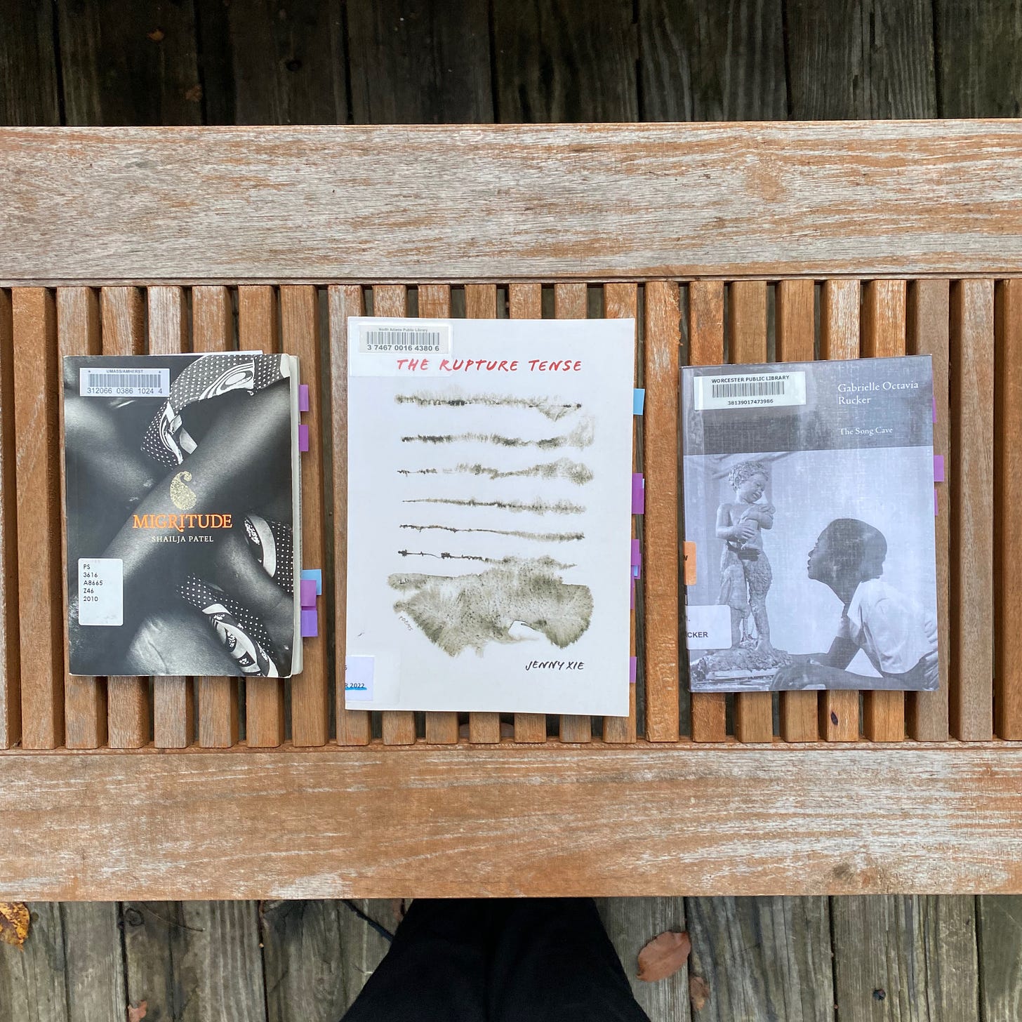 Three poetry collections, all with covers of white and grey, arranged in a line on a porch table.