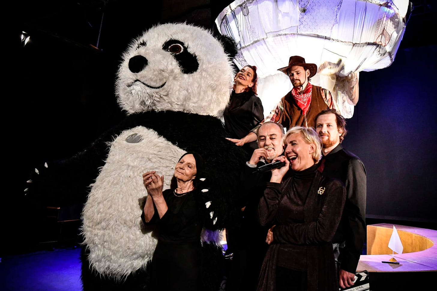 Scene from Negotiating Peace - a group of people sing and dance next to a giant panda.