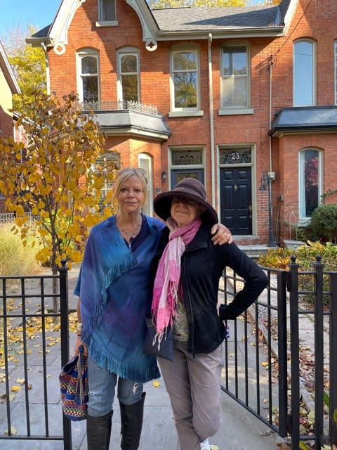 Two women in their 60s, Joyce and Rona Maynard, outside a brick Edwardian rowhouse.