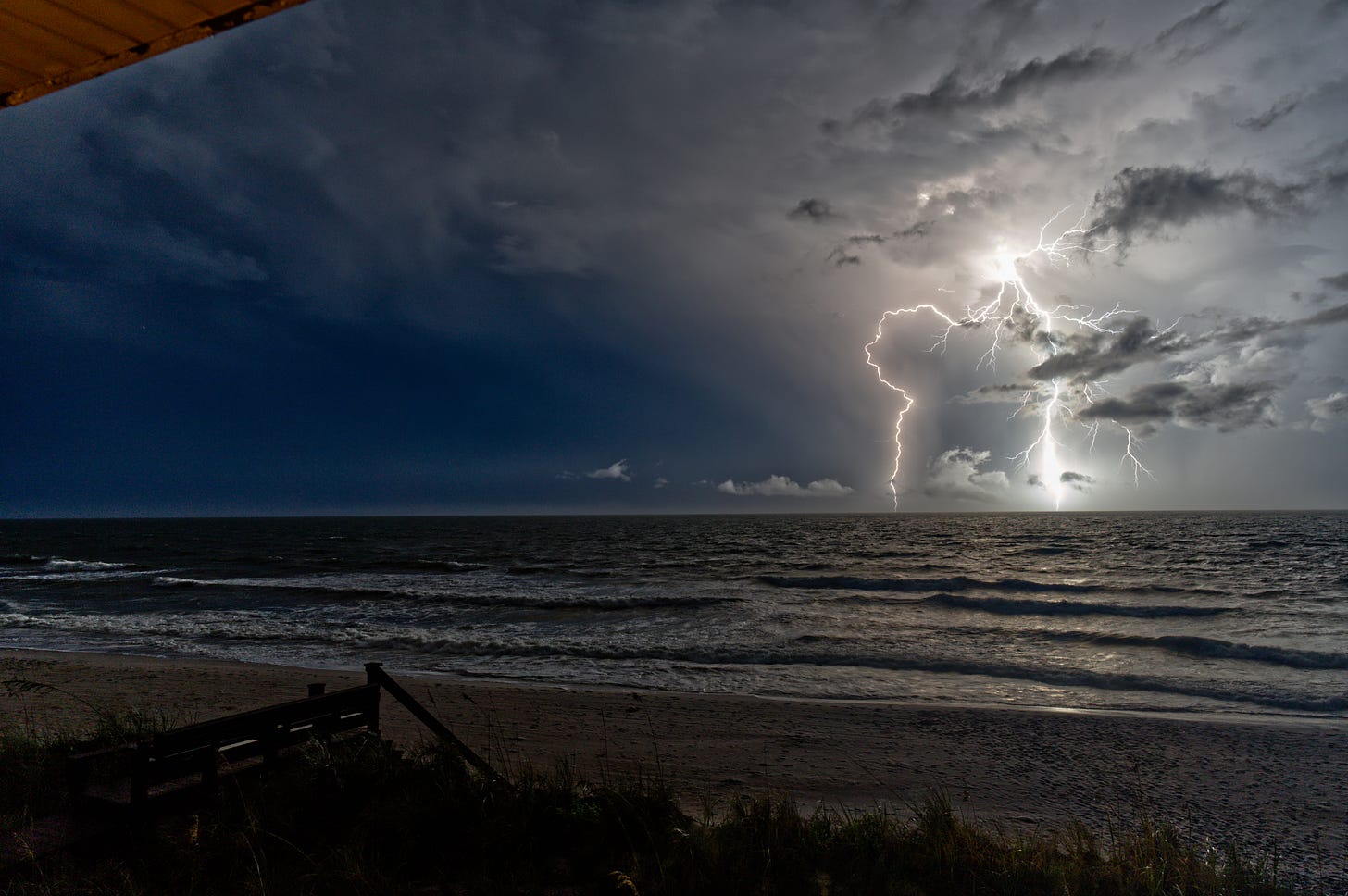 At nighttime, two forks of lightning branch down the horizon over the ocean.