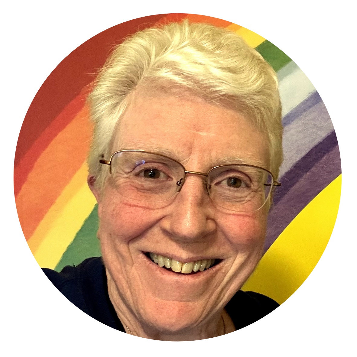 A woman's head shot standing in front of a rainbow decoration