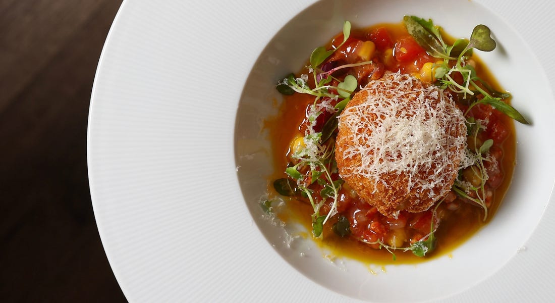 A white plate with an arancini ball with salsa around it in the middle