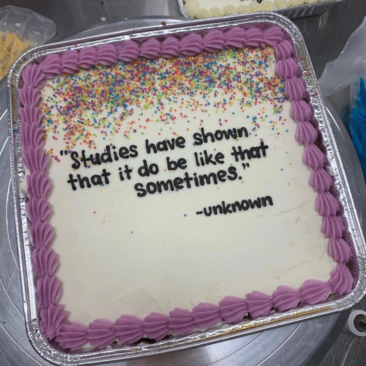 A picture of a square cake in an aluminum container, with white icing and purple frosting piped around the edges. Sprinkles cover the top half of the cake, and in the center of the cake are piped these words: "studies have shown that it do be like that sometimes," which is attributed to unknown.