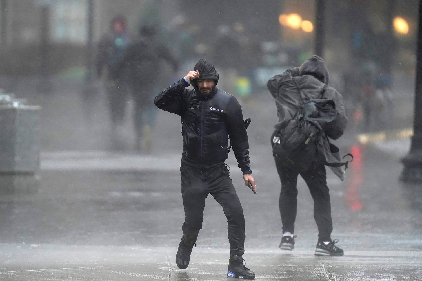 Pedestrians are buffeted by wind and rain.