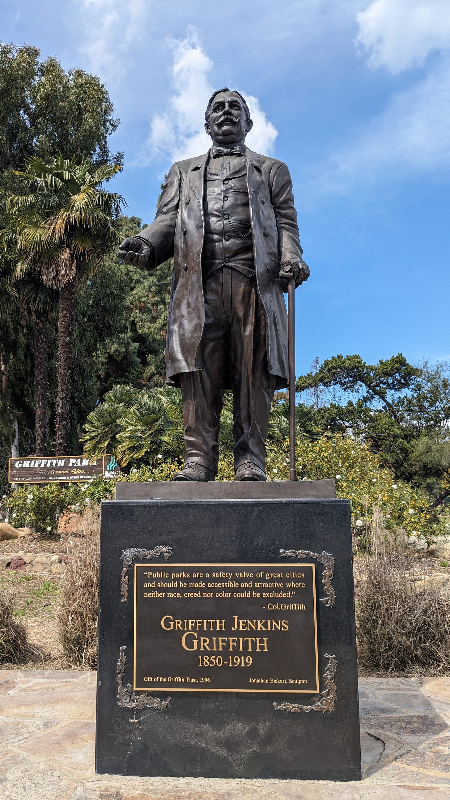 A bronze statue of a middle aged man against a backdrop of trees