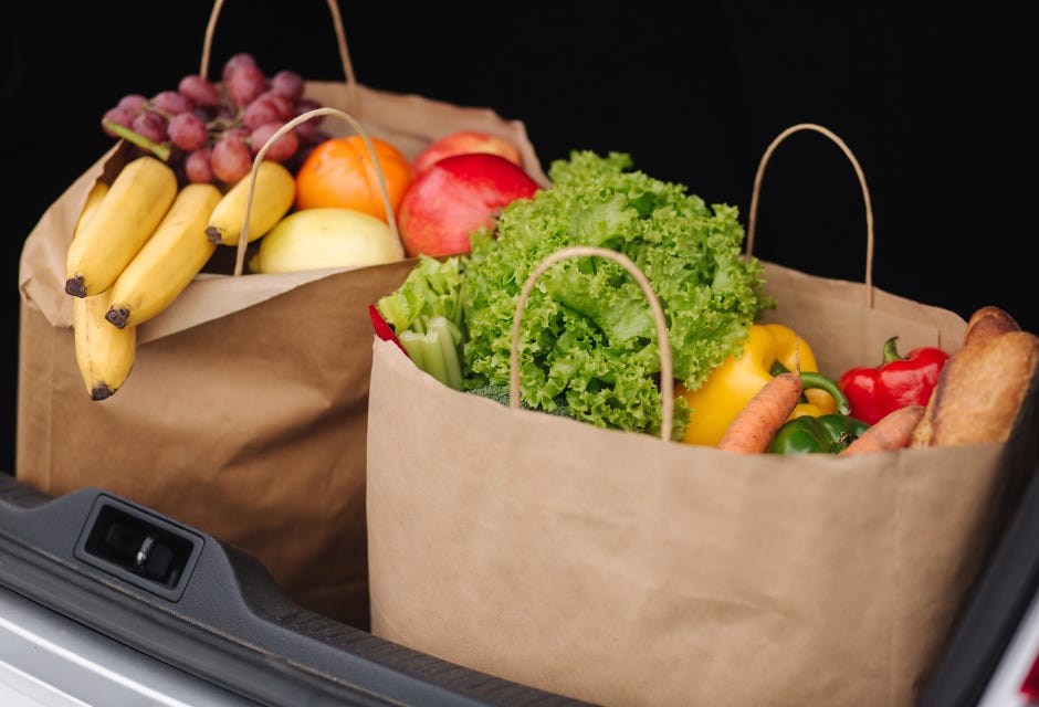 Open trunk of a car with two paper bags of fresh fruits and vegetables.