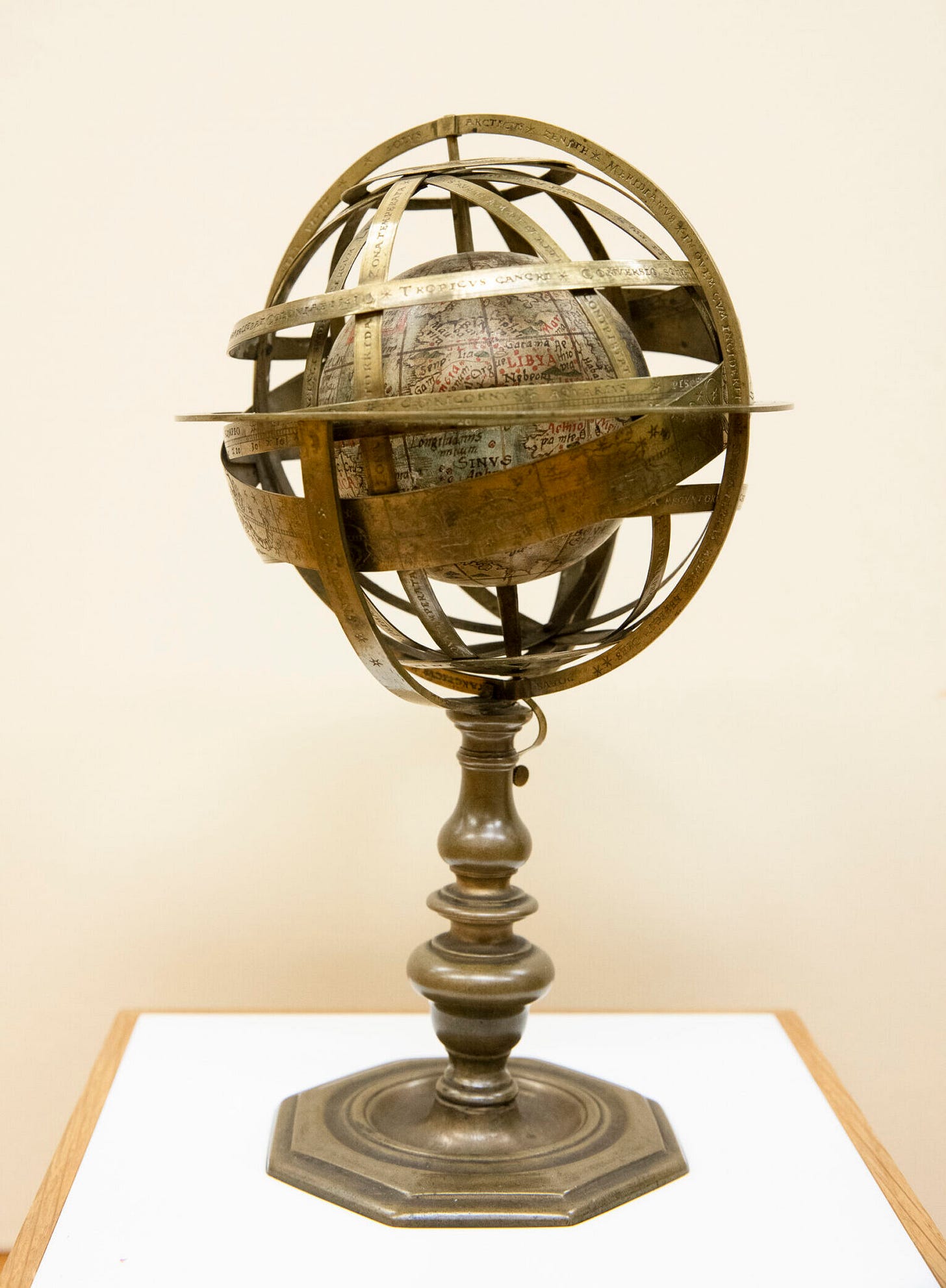 Photograph of an object with a globe at the center and 11 brass rings encircling the globe with a metal octagon base.