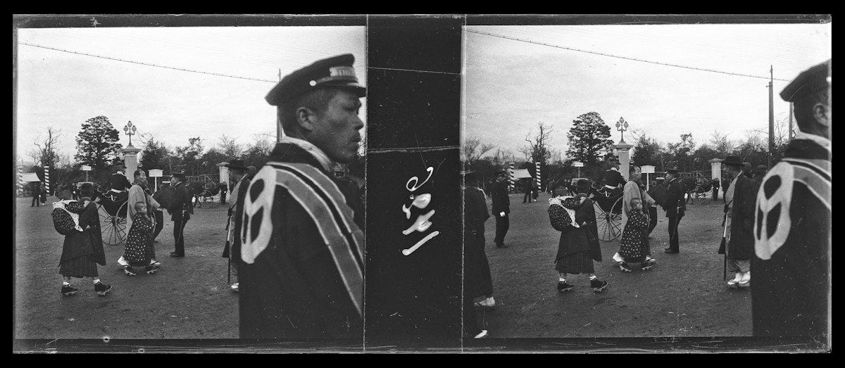 Park entrance with Japanese people in traditional dress and police officers in uniform displaying emblem on back, women carrying parasols near ornate lamp posts."