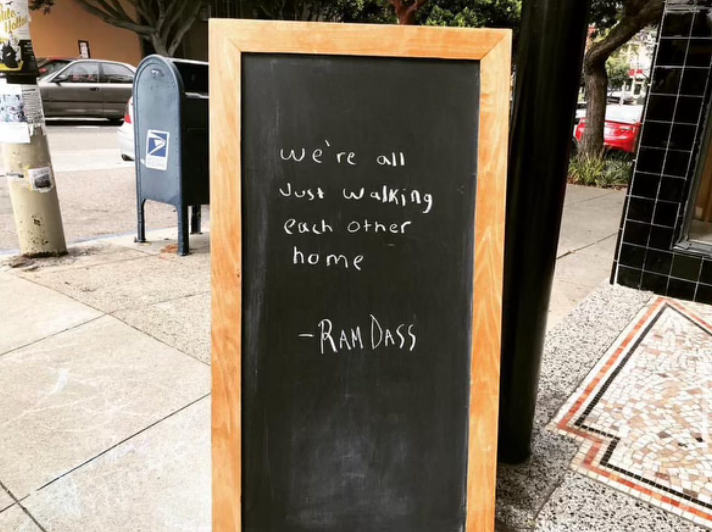 Sign board that says "'We're all just walking each other home' - Ram Dass"